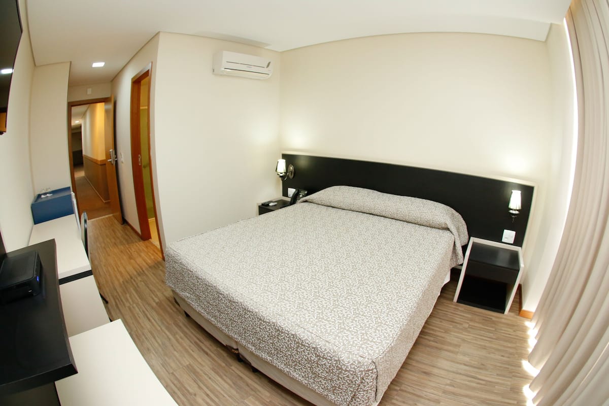A hotel room with a bed, bedside table, and a desk with a chair.