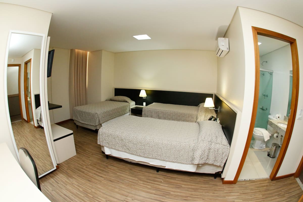 A hotel room with two beds, a desk, a mirror, and a bathroom visible through an open door.