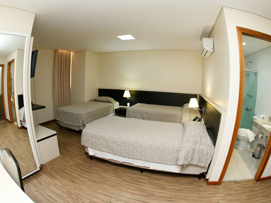 Habitación de hotel con dos camas, un escritorio, un espejo y un baño visible a través de una puerta abierta.