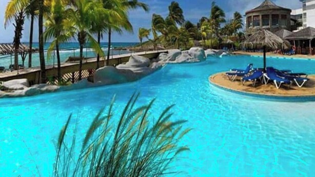 A tropical resort with a clear blue pool, palm trees, and a beach area. - O' calme studio accommodation paradise sea view (Saint François)