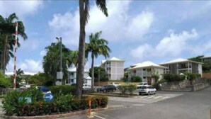A parking area with cars, palm trees, and buildings in the background. - O' calme studio accommodation paradise sea view (Saint François)