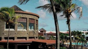 A resort with a stone building, palm trees, and a pool area. - O' calme studio accommodation paradise sea view (Saint François)