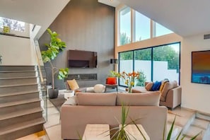 Una sala de estar moderna con una escalera, ventanas amplias y un televisor de pantalla plana.