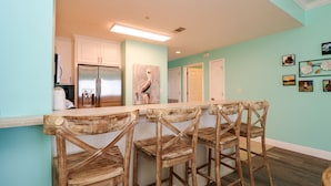 Cozinha com armários brancos, geladeira de aço inoxidável e ilha de madeira com banquetas.