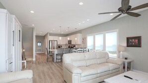 A modern living room with a white leather sofa, a dining area with a table and chairs, and a kitchen in the background.