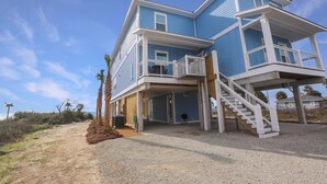 A two-story beachfront house with a covered porch and a staircase leading to the upper level.