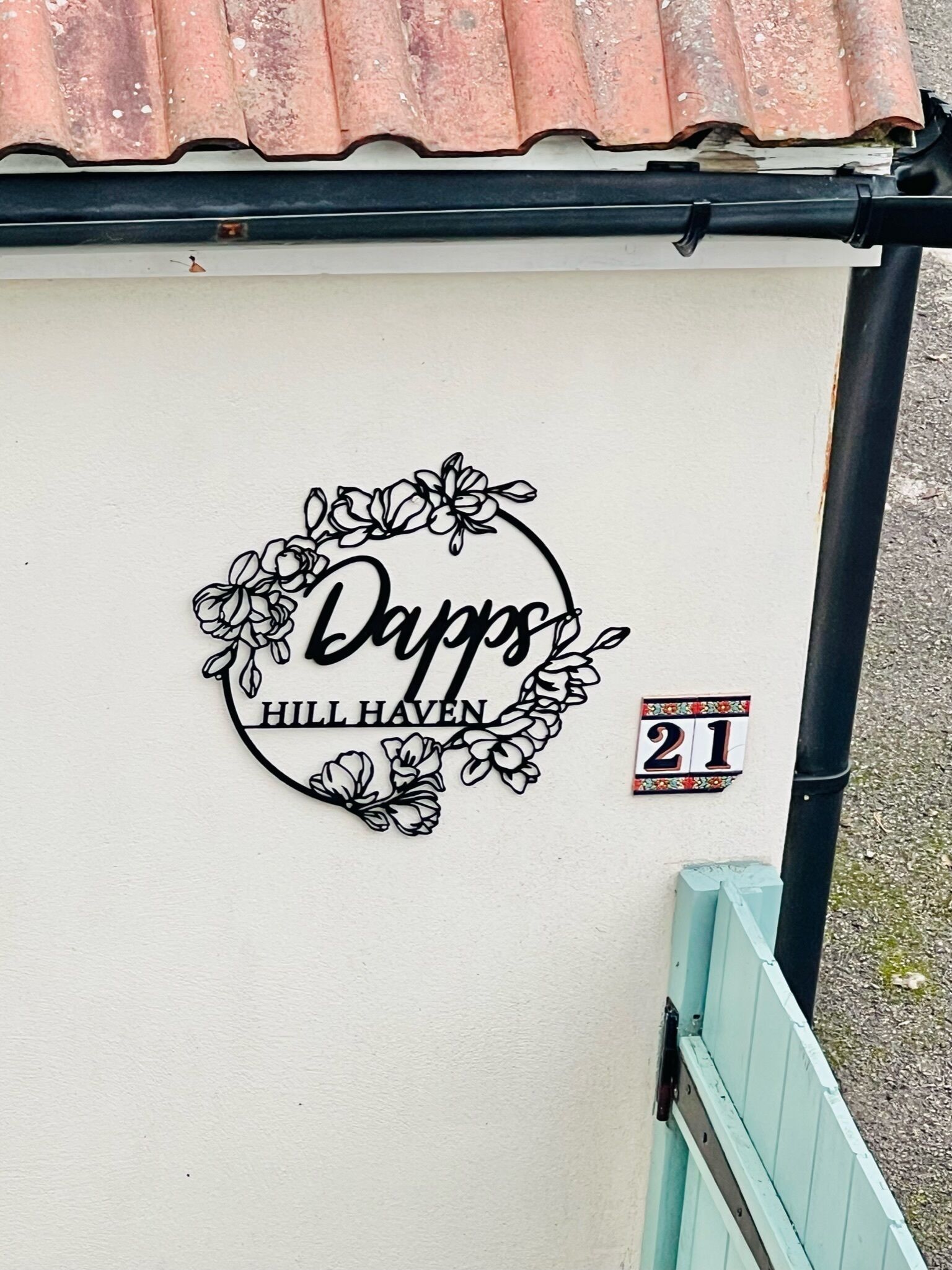 A wall with a decorative metal sign that reads 'Dapp's Hill Haven' and a small sign indicating the number 21.