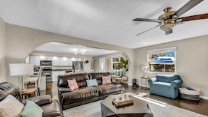 A spacious living room with a leather sofa, a coffee table, and a ceiling fan. - You, Me, and the Sea AMI - Elevated Beach Home with Pool and Spa Steps from Beac (Holmes Beach)