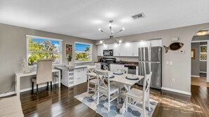 A modern kitchen with white cabinets, a stainless steel refrigerator, and a dining area with a hexagonal rug. - You, Me, and the Sea AMI - Elevated Beach Home with Pool and Spa Steps from Beac (Holmes Beach)