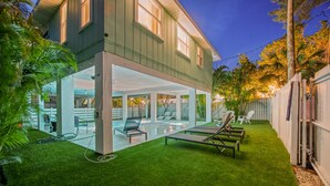 A modern house with a glass-enclosed patio, a swimming pool, and outdoor seating. - You, Me, and the Sea AMI - Elevated Beach Home with Pool and Spa Steps from Beac (Holmes Beach)
