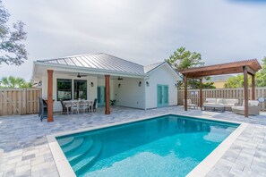 Ein Garten mit Schwimmbecken, Gartenmöbeln und einer überdachten Sitzgelegenheit.
