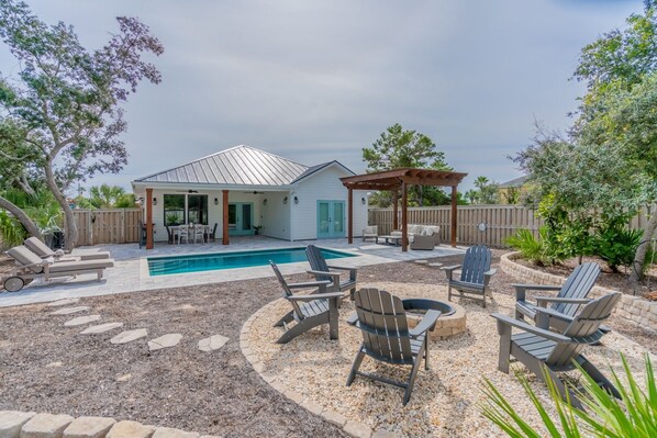 Ein Garten mit Swimmingpool, Liegestühlen und einer überdachten Sitzgruppe.