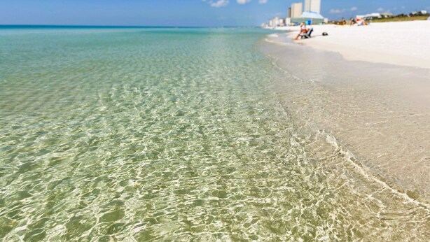 Una playa con aguas poco profundas y cristalinas y una orilla arenosa.