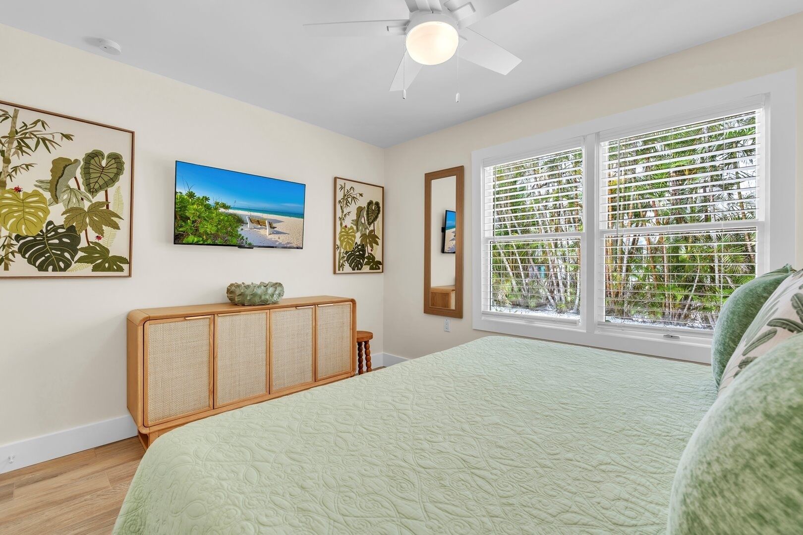 A bedroom with a large bed, a ceiling fan, a window with blinds, and wall art.