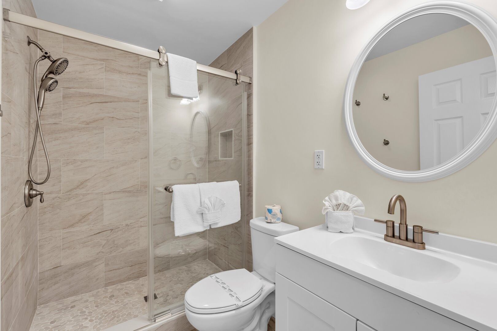 Un baño moderno con ducha de vidrio, inodoro blanco y tocador con lavabo y espejo.