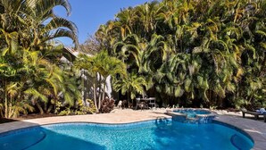 A swimming pool surrounded by palm trees and a patio area with outdoor seating.