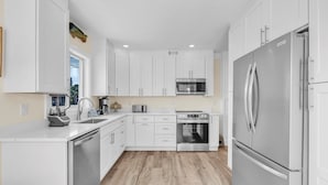 A modern kitchen with white cabinets, stainless steel appliances, and a wooden floor.