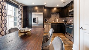 Una cocina moderna con alacenas de madera oscura, electrodomésticos de acero inoxidable y una amplia mesa de comedor de madera.