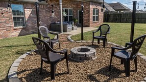 Ein Garten mit Feuerstelle, Gartenmöbeln und einer überdachten Terrasse.