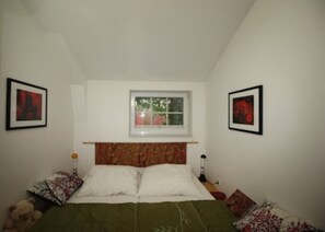 Ein Schlafzimmer mit einem Bett, zwei gerahmten Bildern, einem Fenster und einem Teddybär.