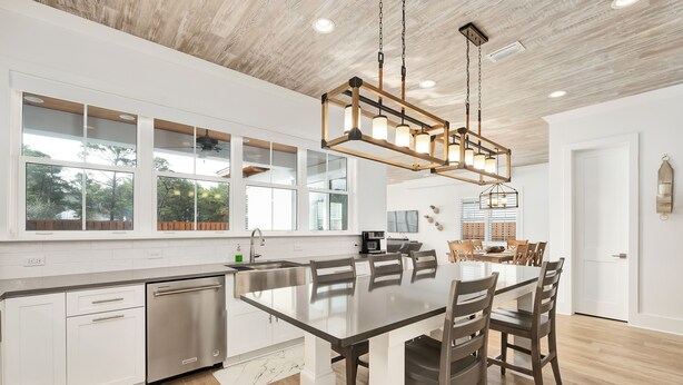 A modern kitchen with a large island, stainless steel appliances, and a farmhouse-style ceiling.