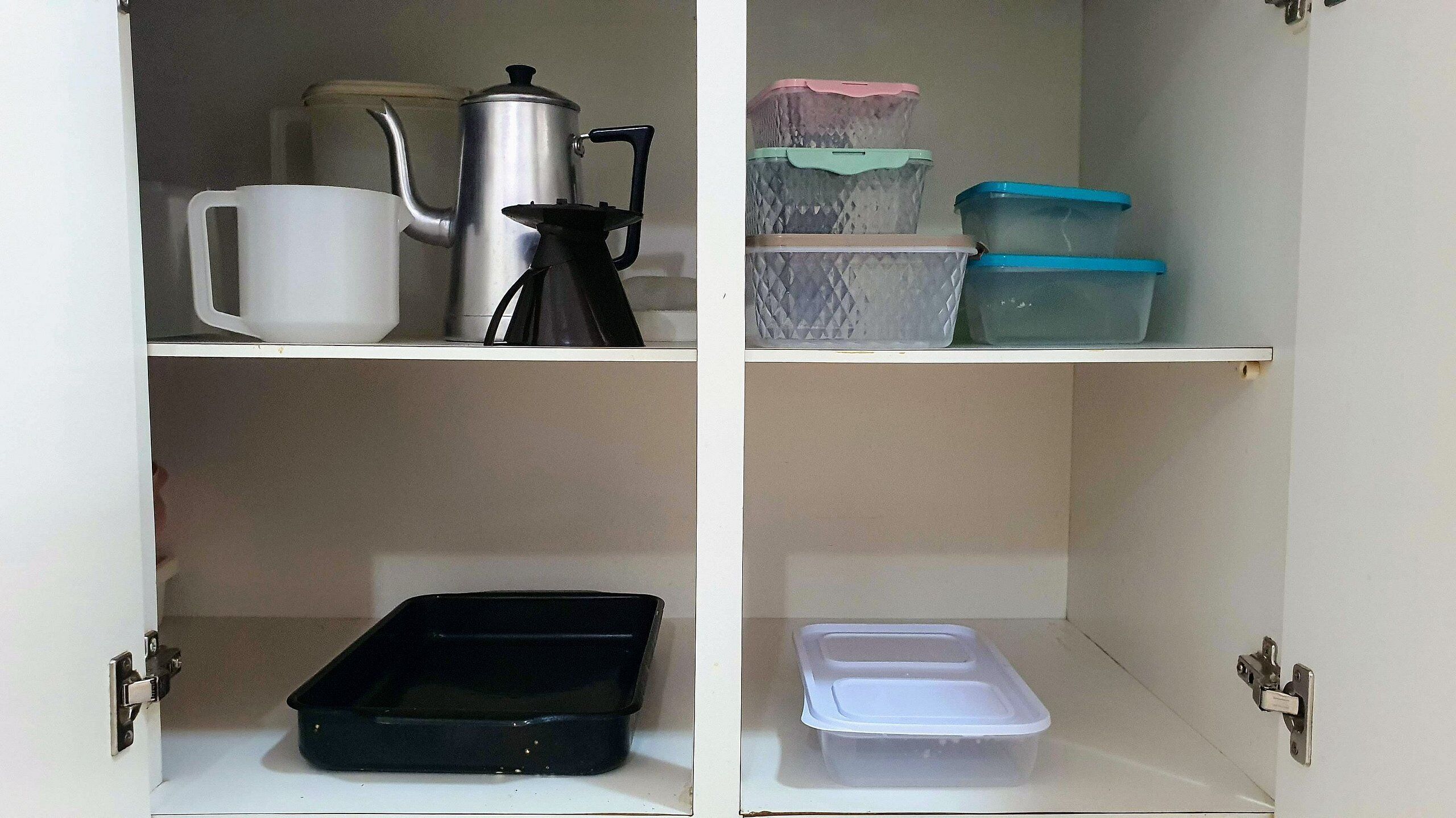 A kitchen cabinet with a kettle, a coffee pot, and storage containers.
