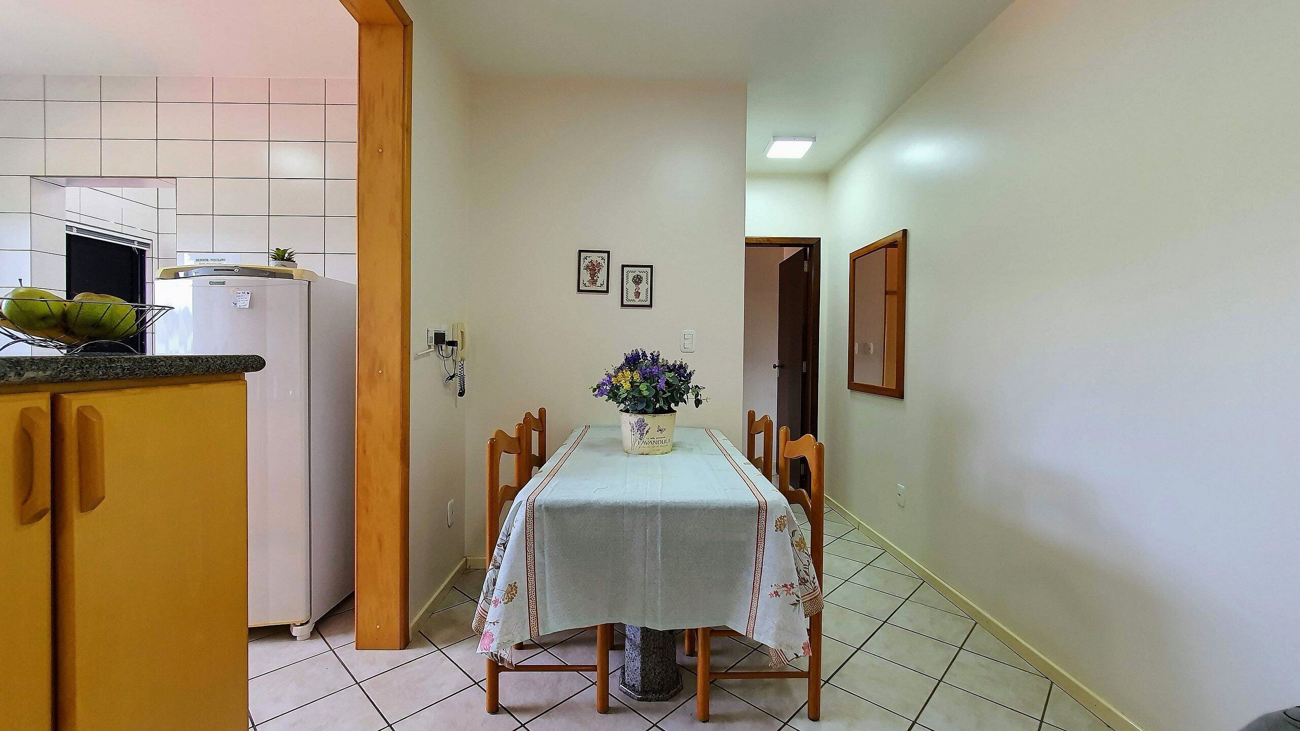 Un pasillo estrecho que conduce a un comedor con una mesa dispuesta para dos personas, un refrigerador y una planta en maceta.