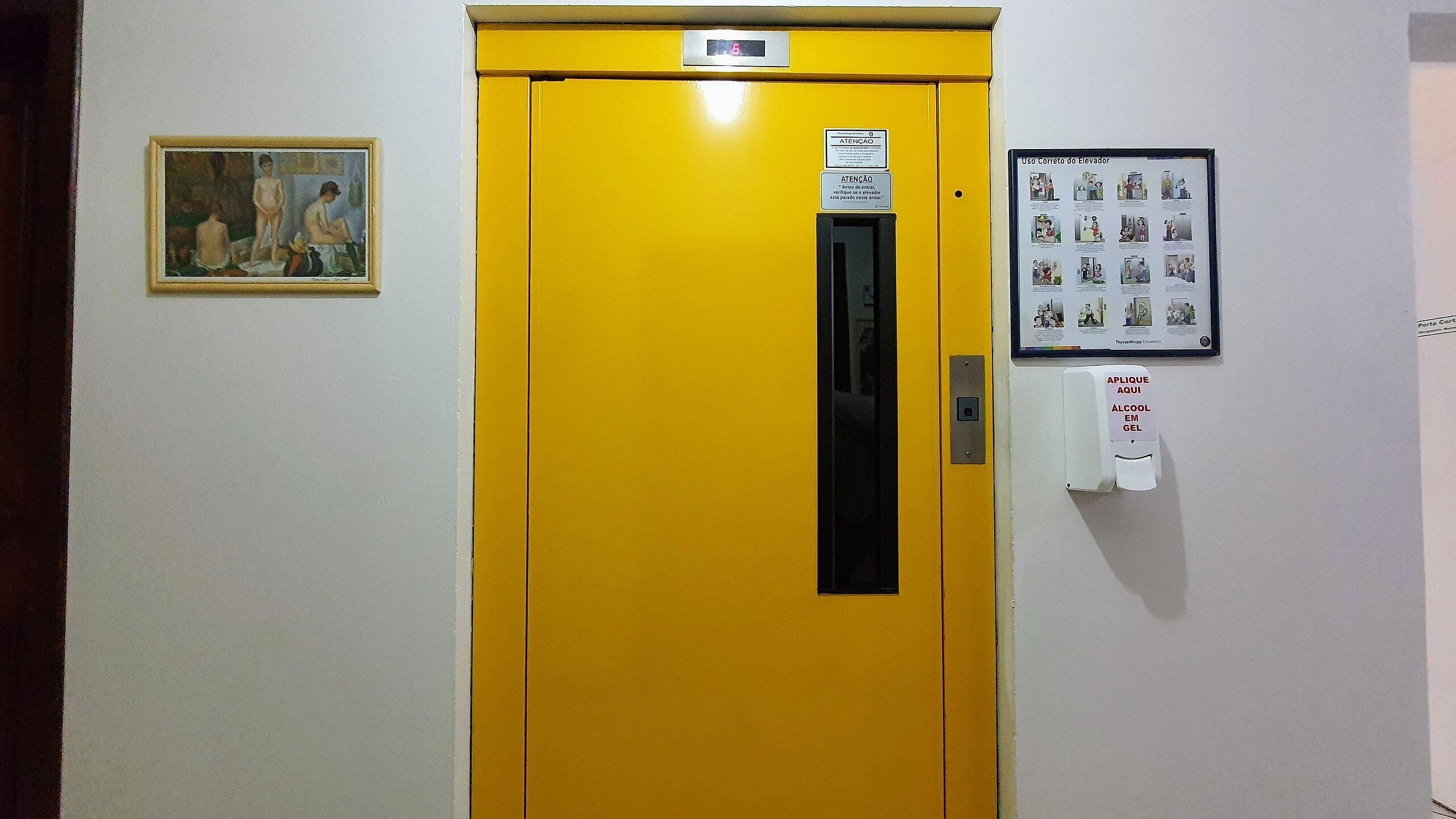 A yellow elevator door with a digital display, a hand sanitizer dispenser, and informational posters on the wall.