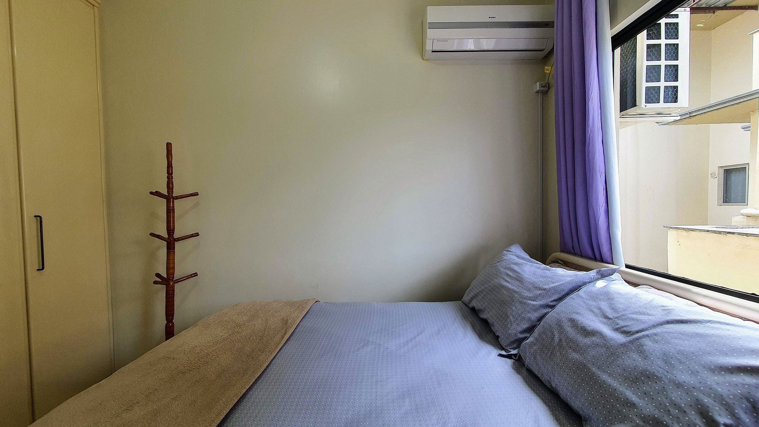 Un dormitorio pequeño y acogedor con una cama individual, un armario y un ventanal con cortinas moradas.