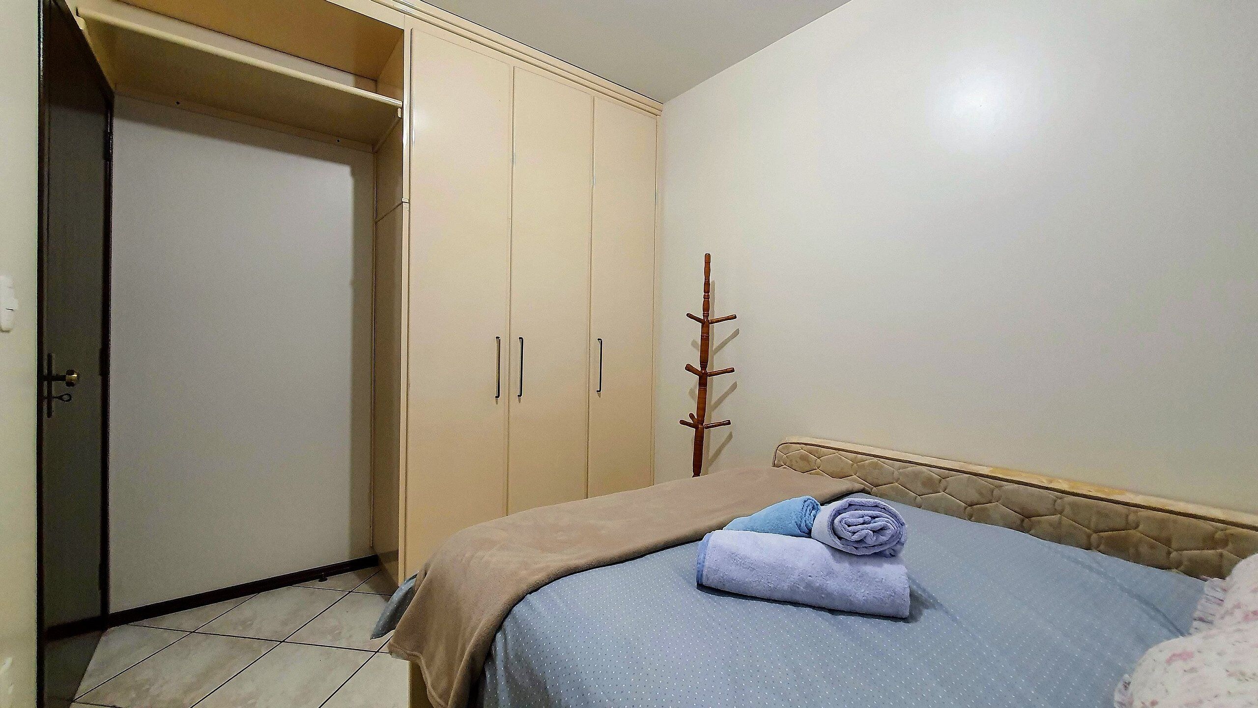 A bedroom with a bed, a wardrobe, and a wooden coat rack.