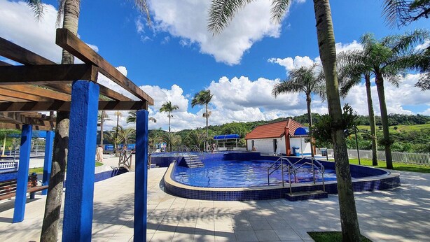 Zona de piscina con un espacio de descanso techado, palmeras y un edificio de techo rojo.