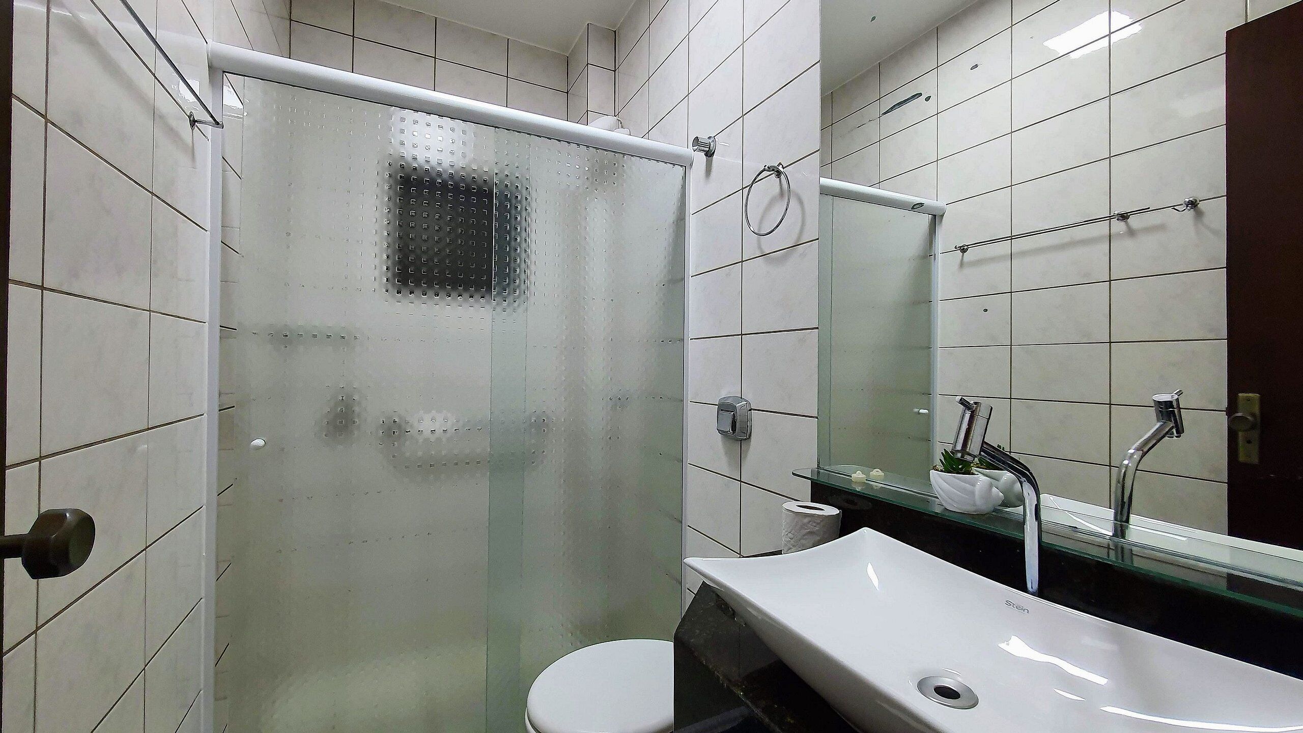 A bathroom with a glass shower enclosure, a white toilet, a sink with a mirror, and tiled walls.