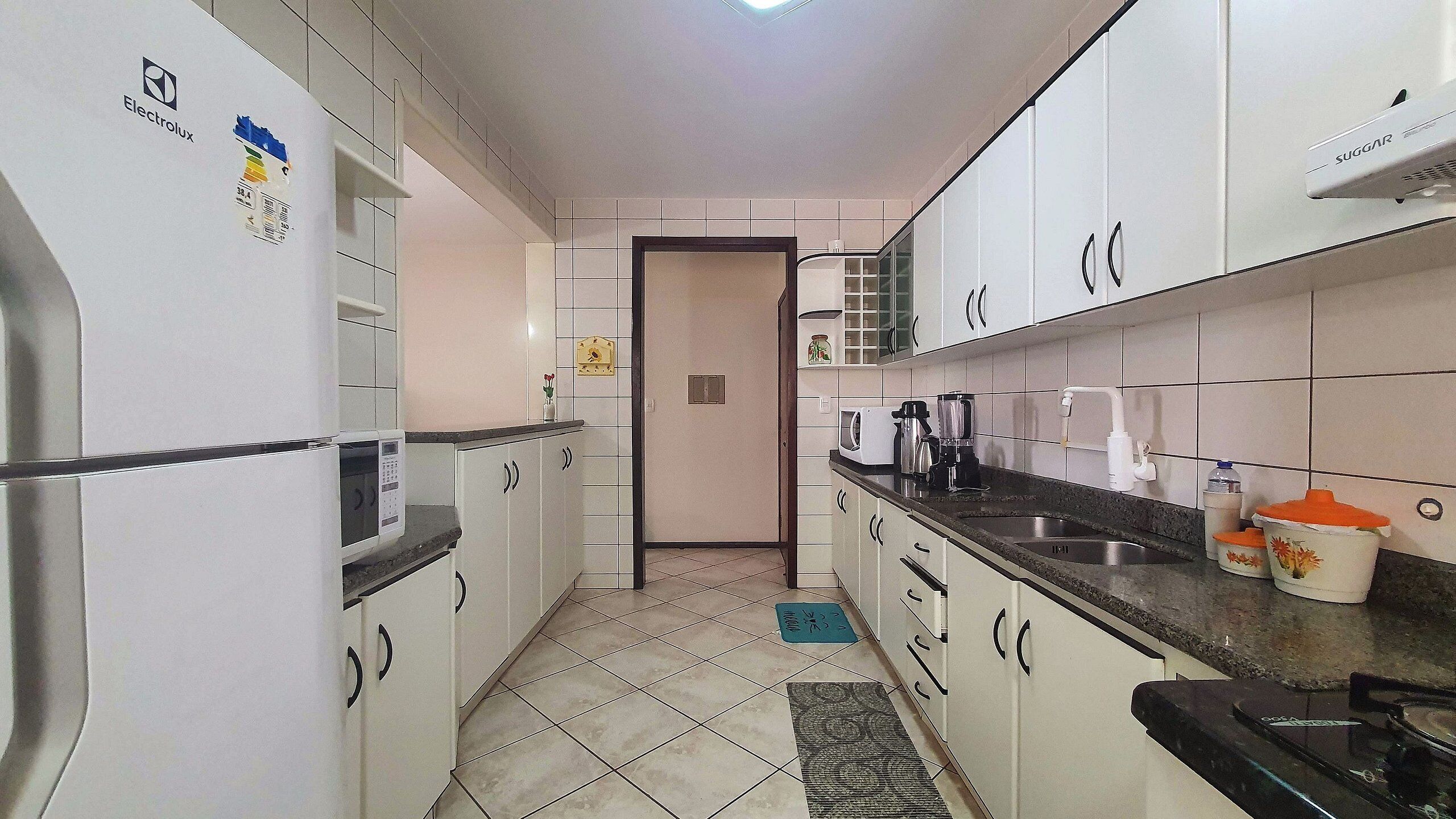 A narrow kitchen with white cabinets, a microwave, a coffee maker, and a sink.