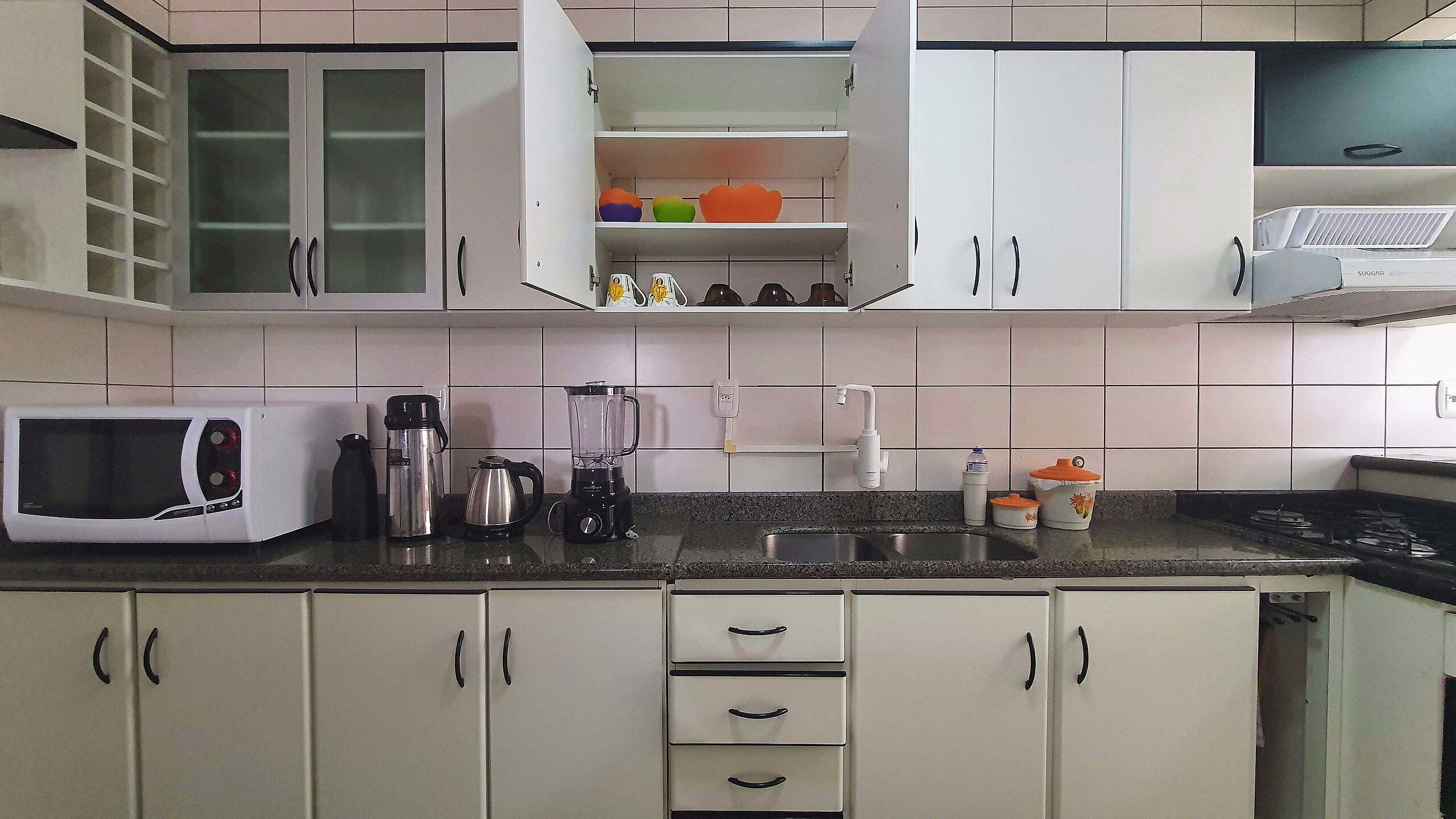 Une cuisine avec des armoires blanches, un four à micro-ondes, une machine à café et un mixeur sur le plan de travail.