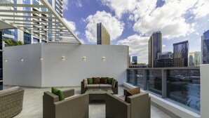Eine Dachterrasse mit Korbmöbeln, einem Glastisch und Blick auf die Stadtlandschaft.