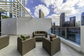 Una terraza en la azotea con mobiliario de mimbre, una mesa de cristal y vistas a la ciudad.