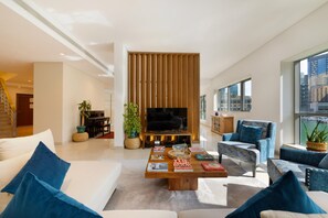 Una sala de estar moderna con un televisor de pantalla plana, un piano y una mesa de centro con libros.