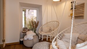 Una habitación acogedora con una silla colgante, un banco acolchado y una mesita con velas y un jarrón.