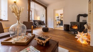 Una sala de estar acogedora con chimenea, una mesa de centro de madera con un juego de ajedrez, un sillón colgante y un jarrón con plantas secas.