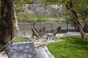 A hammock, two folding chairs, a small table with glasses, and a view of a river and mountains. - Historic winegrower's house in the Wachau wine region on the Danube with pool & sauna (Oberarnsdorf)