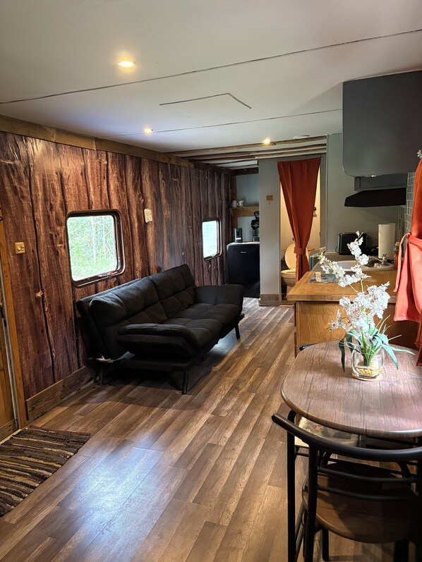 A compact living space with a sofa, a dining table with chairs, a small kitchen area, and a window.