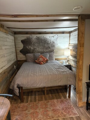 A bedroom with a wooden headboard, patterned bedding, a decorative rug, and a bedside lamp.