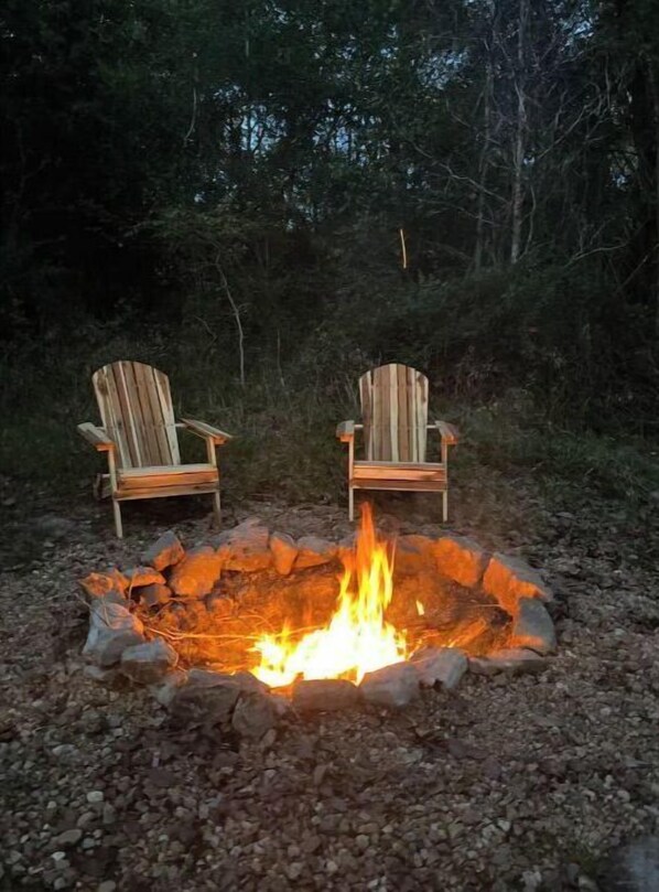 Two Adirondack chairs facing a campfire in a forested area. - Cabin 1 Cozy cabin close to Sam Houston Park (Huntsville)