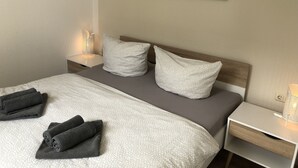Una cama bien tendida con una colcha estampada, dos almohadas y toallas dobladas.
