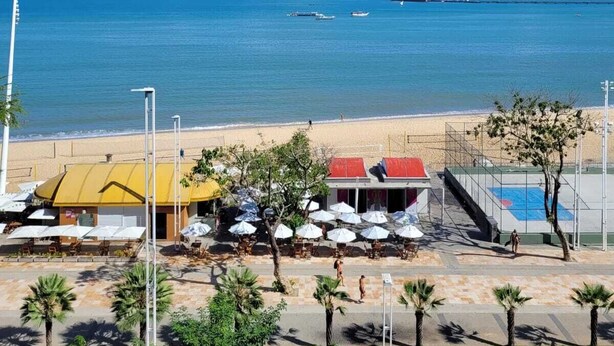 Vista de la playa con cielo despejado, arena y algunos sombrillas y edificios.