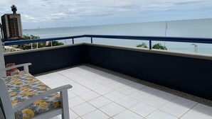 Un balcón con una silla blanca y una mesa, con vistas a un cuerpo de agua y un horizonte urbano distante.
