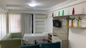 Habitación de hotel con cama, escritorio, silla, televisor y estante con botellas decorativas.