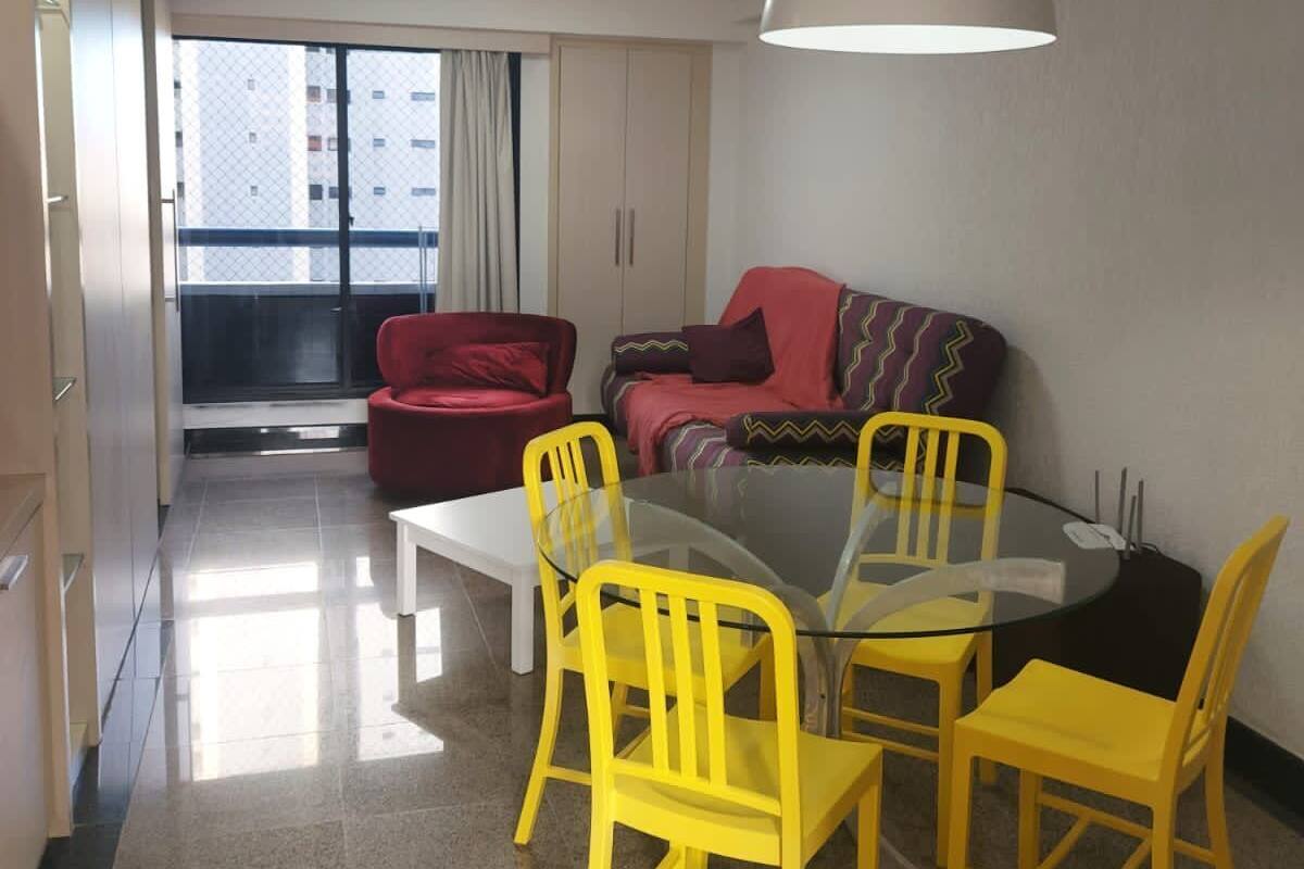 A modern living room with a glass dining table, yellow chairs, a red sofa, and a large window.