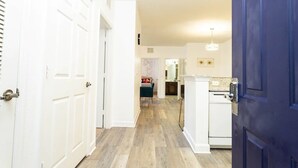 Un couloir avec des portes blanches, un coin cuisine équipé d’un réfrigérateur et un espace repas avec une table et des chaises.