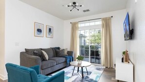 Un salon moderne avec un canapé gris, des fauteuils bleus, une table basse ronde et un téléviseur fixé au mur.